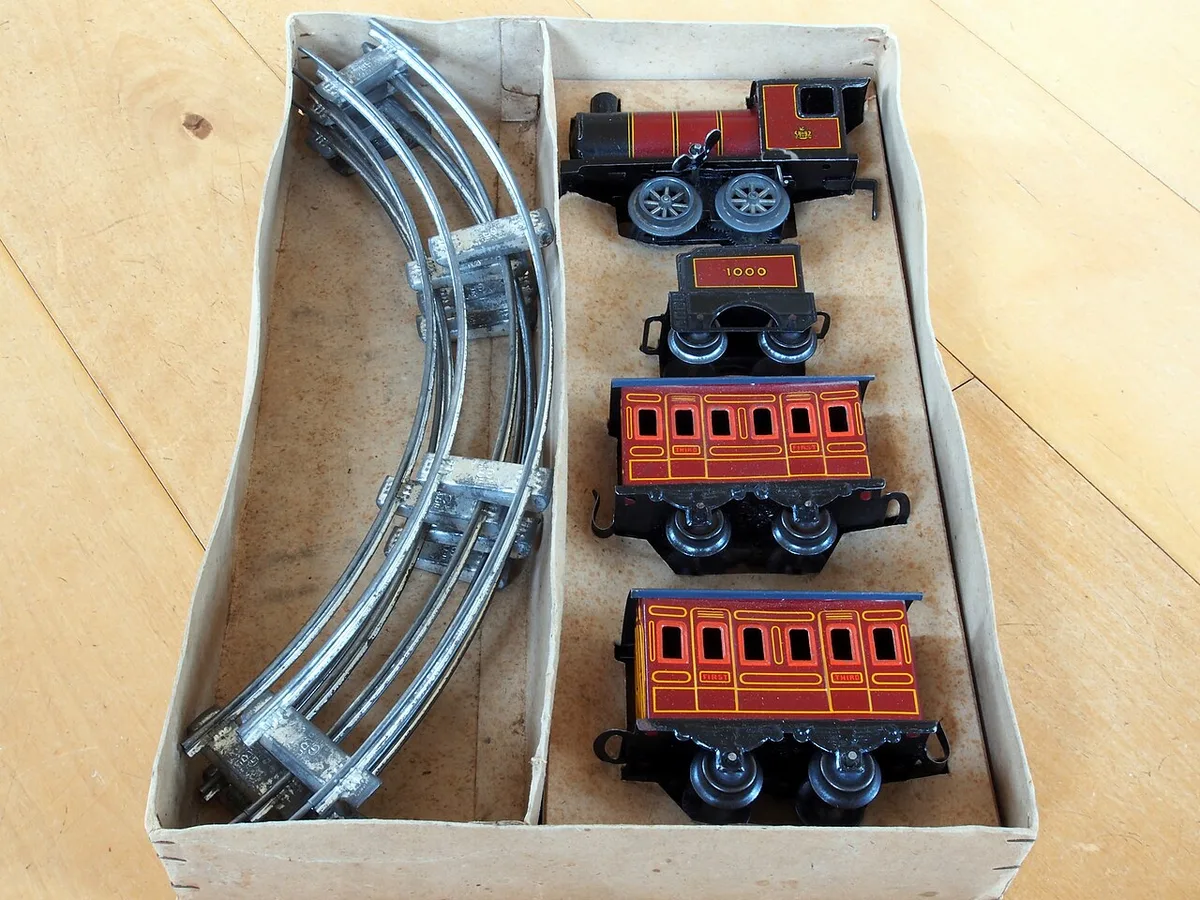Een blikken opwindtrein met locomotief, twee rijtuigen en gebogen railstukken ligt in de oorspronkelijke kartonnen doos.